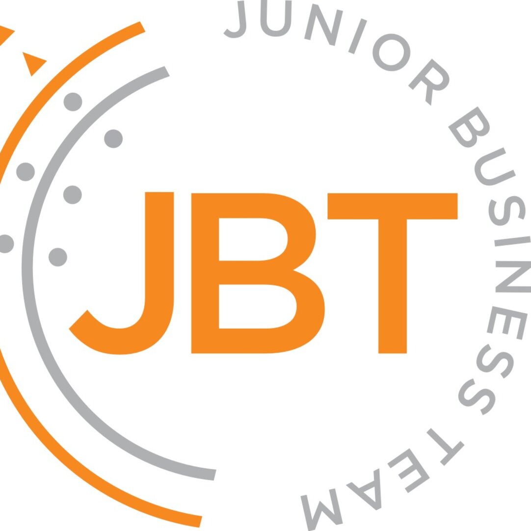 Logo des Junior Business Teams (JBT): Orangefarbener Schriftzug „JBT“ in der Mitte, umgeben von einem kreisförmigen, grauen Schriftzug „Junior Business Team“. Links rahmen ein orangefarbener und ein grauer Bogen mit grauen Punkten und zwei kleinen orangefarbenen Dreiecken das Logo ein.