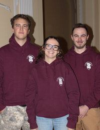 Foto: Drei Personen tragen bordeauxfarbene Hoodies mit dem Logo der Universität Hohenheim und der Aufschrift 'VS'. Sie stehen vor einem neutralen Hintergrund in einem Innenraum.